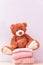 Teddy bear sits near stack of winter or autumn womens clothes. Pile of rose knitted cozy warm pink sweaters or pullover on wooden