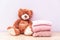 Teddy bear sits near stack of winter or autumn womens clothes. Pile of rose knitted cozy warm pink sweaters or pullover on wooden