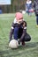 Teen age girl football player holding ball with hands while sitting on an artificial green field