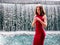 Teen ager girl in high fashion red dress posing in water, water fall behind her back. Prom photoshoot in beautiful location Young