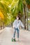 Teen Asian girl in white shirt and jeans is practicing for a play. Surf skating along the beachfront promenade behind many coconut