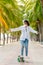 Teen Asian girl in white shirt and jeans is practicing for a play. Surf skating along the beachfront promenade behind many coconut