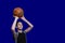 Teen in a black T-shirt is preparing to throw a basketball. Isolated on blue background. Copy space. Blank for sports poster