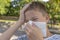 Teen boy blows his nose in a paper handkerchief and touches his head