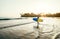 Teen boy with blue and yellow surfboard entering the waves for surfing with sunset rays on palm trees grove. Happy childhood and