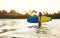 Teen boy with blue and yellow surfboard entering the waves for surfing with sunset rays on palm trees grove. Happy childhood and