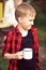 Teen boy kid in checkered shirt holding a cup of drink. Travel, hike, vacation, camping concept.