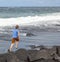 Teen boy runs along a black volcanic beach