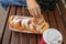 A teen boy sitting on a bench in park and eating beignet pastries, donuts and drinking coffee or tea from a takeaway box and cup,