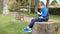 Teen boy with smart phone listening or talking while sitting on stump in british park. teenager and social media concept