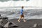 Teen boy walks along a black volcanic beach