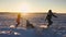 Teen daughter and mother pulling little son on sledge, running. Silhouette family playing in winter time. Active healthy