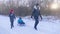 Teen daughter and mother pulling little son on sledge, running. Silhouette family playing in winter time. Active healthy