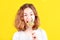 Teen girl angry bites a multi-colored round lollipop on yellow background