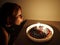 Teen girl blowing on candles on cake in dark room, thirteenth birthday