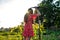 Teen girl with brunette loose hair in red dress standing back to the camera, leaned on a rake, resting while working in