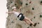 A teen girl climbing on a rock wall leaning back against the rope.