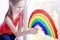 Teen girl draws a rainbow on the window a symbol of the fight against coronavirus