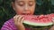 Teen girl eats a sweet, juicy watermelon on the background of greenery. The child enjoys a big slice of watermelon.