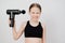 Teen girl grimaces and holds a massage gun. medical-sports device