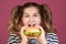 Teen girl holding the beef burger sandwich with happy face and hungry open mouth on isolated pink background