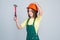 teen girl laborer in protective helmet and uniform on grey background use hammer, worker