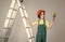 teen girl laborer in protective helmet and uniform on ladder with painting brush, renovation