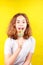 Teen girl licks a multi-colored round lollipop on yellow background
