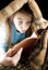 Teen girl reading book under blanket