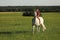 Teen girl ride on white horse without saddle on meadow in late afternoon, sunset time