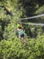 Teen girl riding a zipline through the forest. View from behind