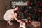Teen girl takes a new year gift from under the Christmas tree happily smiling crouching beside the Christmas decorated fireplace