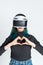 Teen girl using vr helmet shows heart gesture with hands on white background. Virtual love concept. The concept of the