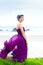 Teen girl wearing purple gown on grassy knoll overlooking ocean