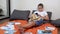 Teen in Glasses with a Smartphone in Hands and Open Book Studying Online at Home