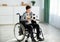 Teen handicapped soccer player with ball and trophy sitting in wheelchair, feeling depressed over his injury at home