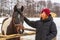 Teen redhead girl patting horse at ranch in snowy day. Winter weekend at farm, trip to countryside. Healthy lifestyle, active