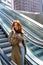 Teen redhead girl talking on cell standing on escalator.