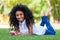 Teenage black girl using a phone, lying on the grass - African p