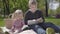 Teenage blond boy sitting on blanket in the park reading the book to her little sister in pink dress sitting near. The