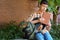 A teenage boy, being a student, is sitting on a bench near the school building, he takes a book or other school supplies out of