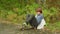 Teenage boy in casual clothing sitting on longboard in beautiful park