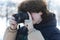 A teenage boy with curly long hair takes a picture with a digital SLR camera. Winter photo shoot outdoors