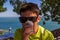 A teenage boy with dark glasses drinks coffee from a disposable Cup against the background of the sea.