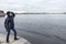 Teenage boy is on granite embankment of Neva river, view at the Peter and Paul Fortress from water, winter season in Saint-