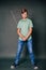 A teenage boy in a green T-shirt and jeans holds a medieval sword in his hands. Studio photo on a gray background