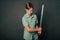 A teenage boy in a green T-shirt and jeans holds a medieval sword in his hands. Studio photo on a gray background