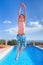 Teenage boy jumping high above blue swimming pool