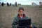 A teenage boy with a laptop grazes goats in a field. A goat herder in a field with a laptop communicates over the Internet.