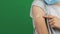 Teenage boy with medical protective mask showing to his arm with plaster after vaccination over green screen background